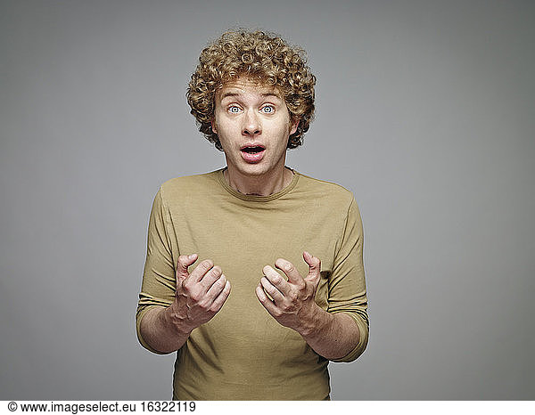Portrait of astonished blond man in front of grey background
