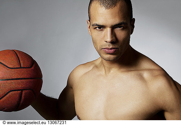 Portrait of athlete holding basketball while standing against gray background