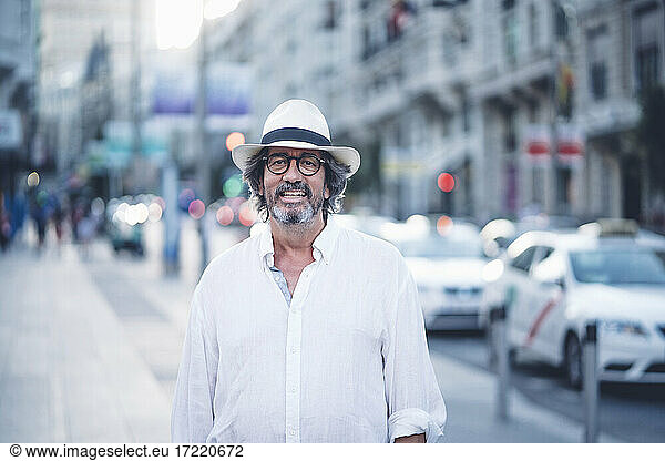 Portrait of attractive senior man with white clothing and hat posing at camera in street of Madrid