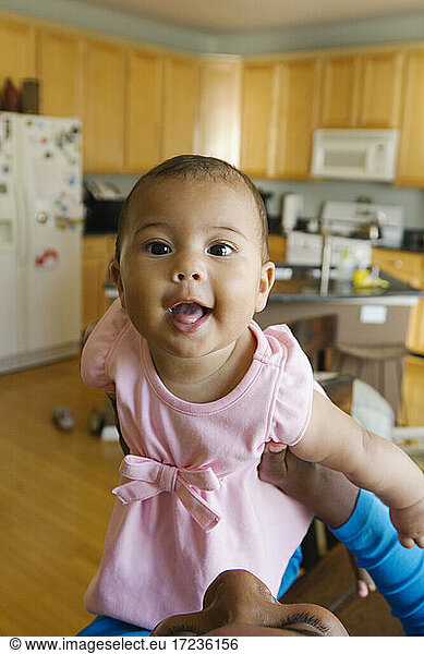 Portrait of baby girl in kitchen looking at camera smiling