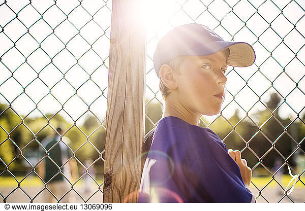 Portrait of baseball player standing by fence in dugout