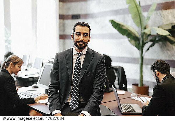 Portrait of bearded businessman sitting on desk in office