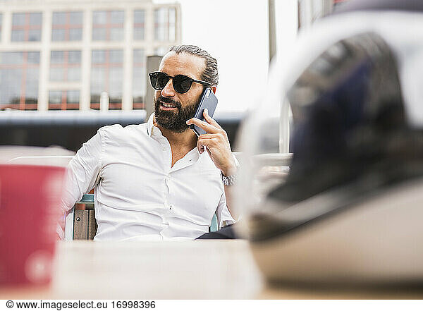 Portrait of bearded businessman wearing sunglasses talking outdoors on smart phone