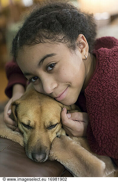 Portrait of biracial eleven year-old girl snuggling a small brown dog