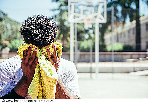 Portrait of Black African-American boy drying his sweat from his forehead with a towel on an urban basketball court.