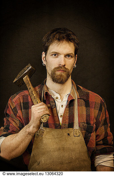 Portrait of blacksmith carrying hammer while standing against black background