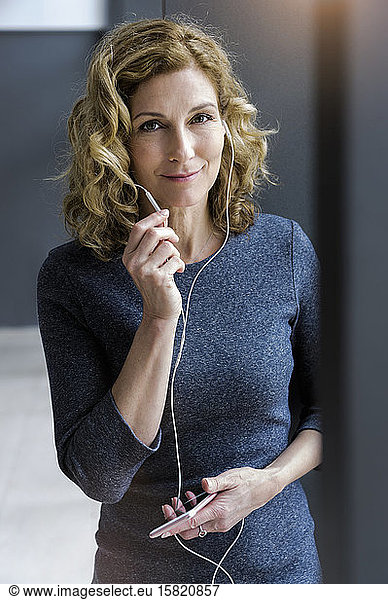 Portrait of blond businesswoman with earphones and smartphone in office
