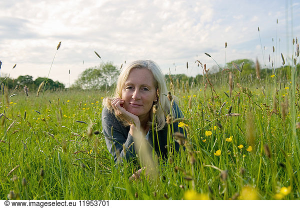 Portrait of blond woman lying on her front on a meadow  hand on chin  smiling at camera.