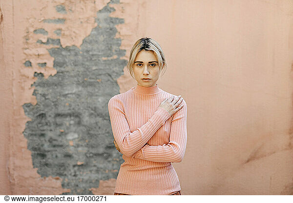 Portrait of blond woman wearing pink turtleneck pullover in front of a pink wall