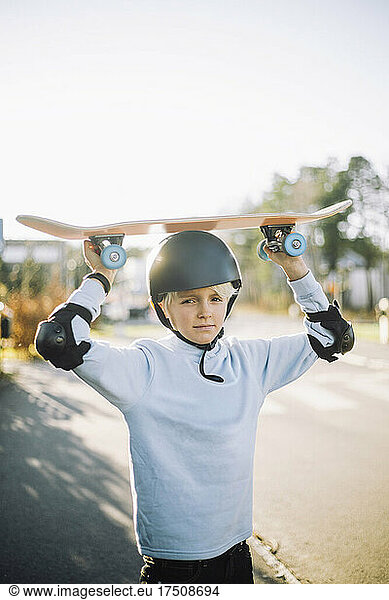 Portrait of boy carrying skateboard on head