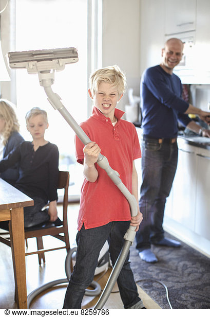 Portrait of boy clenching teeth while holding vacuum cleaner at home
