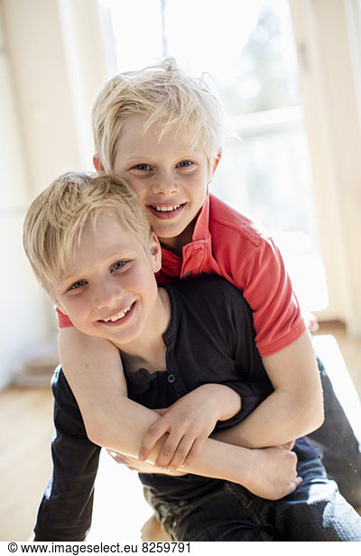 Portrait of boy embracing brother from behind in house