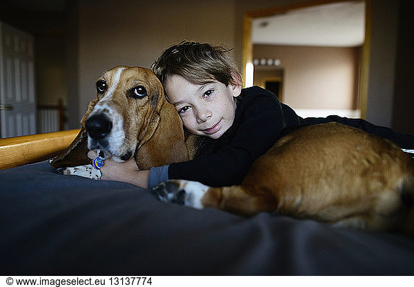 Portrait of boy embracing dog while lying on bed
