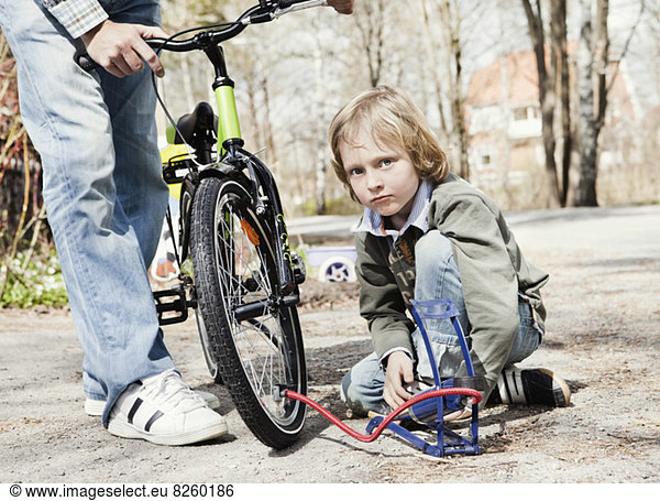 Portrait of boy filling bicycle tire with foot pump while father standing on road
