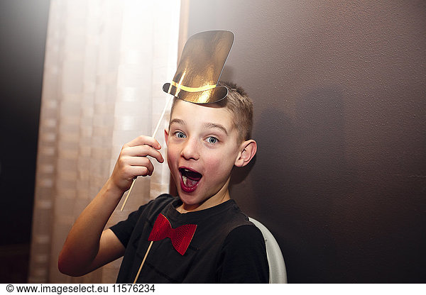 Portrait of boy holding bow tie and top hat stick masks posing at party