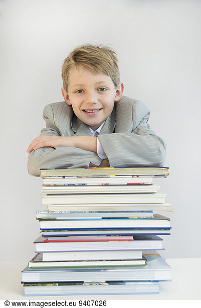 Portrait of boy leaning on stack of books  smiling