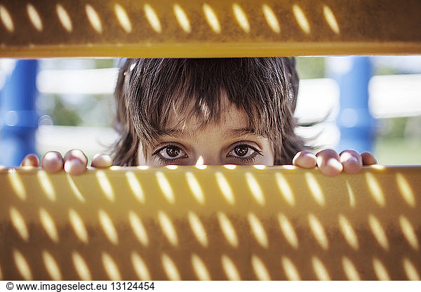Portrait of boy peeking through outdoor play equipment
