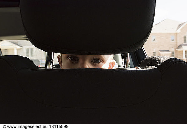 Portrait of boy peeking through seat in car