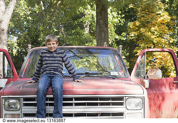 Portrait of boy sitting on hood of pickup truck in woods