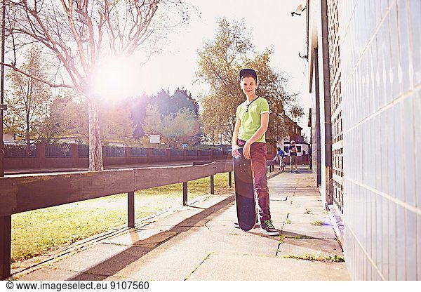 Portrait of boy standing on pavement holding skateboard