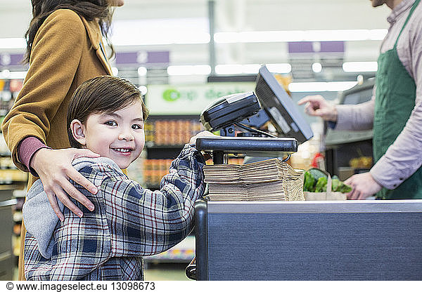 Portrait of boy standing with mother standing counter at supermarket