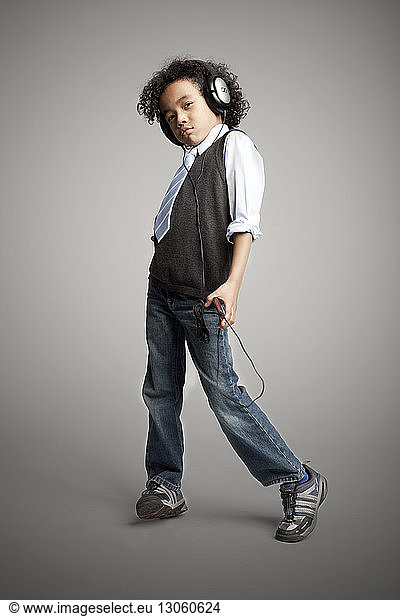 Portrait of boy wearing headphones while standing against gray background