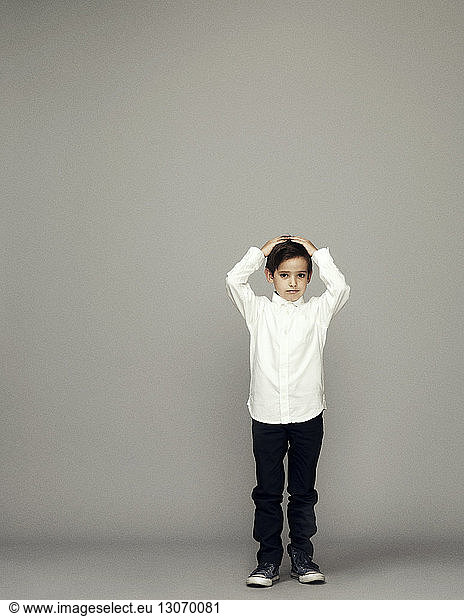 Portrait of boy with hand in hair standing against gray background