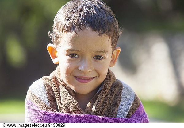 Portrait of boy with wet hair wrapped in towel in garden
