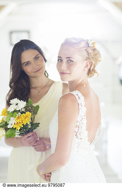 Portrait of bride and bridesmaid with bouquet of flowers in domestic room