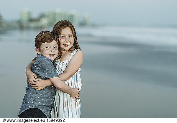 Portrait of brother and sister hugging at the beach at dusk