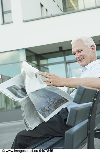 portrait of business man sitting on a bench reading newspaper