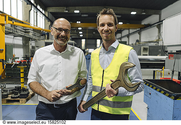 Portrait of businessman and man in reflective vest with large wrenches in a factory