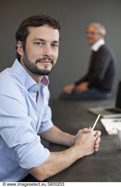 Portrait of businessman holding pen with colleague in background