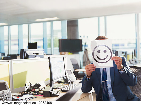 Portrait of businessman holding smiley face printout over his face in office