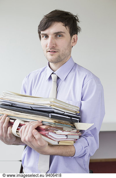 Portrait of businessman holding stack of files in office  smiling