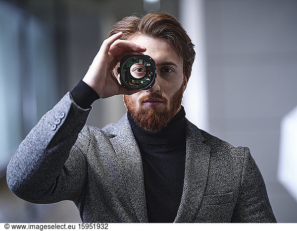 Portrait of businessman looking through an object in modern office