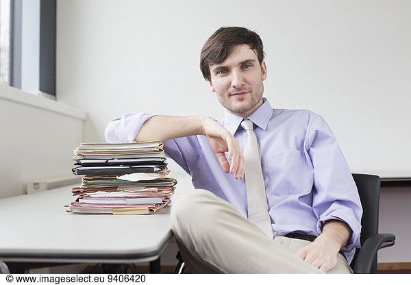 Portrait of businessman sitting in office with stack of files