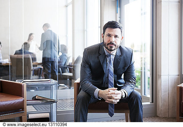 Portrait of businessman sitting with hands clasped in office