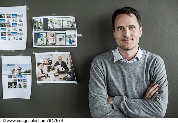 Portrait of businessman standing arms crossed against wall in office