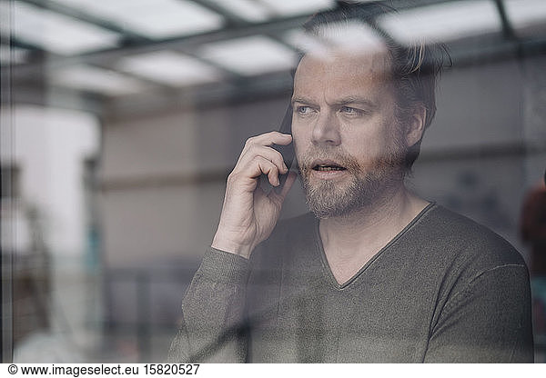 Portrait of businessman uon the phone behind windowpane