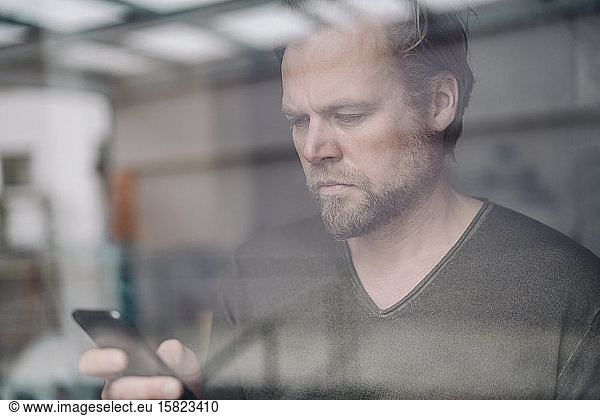 Portrait of businessman using cell phone behind windowpane