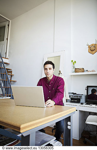 Portrait of businessman using laptop at table in creative office