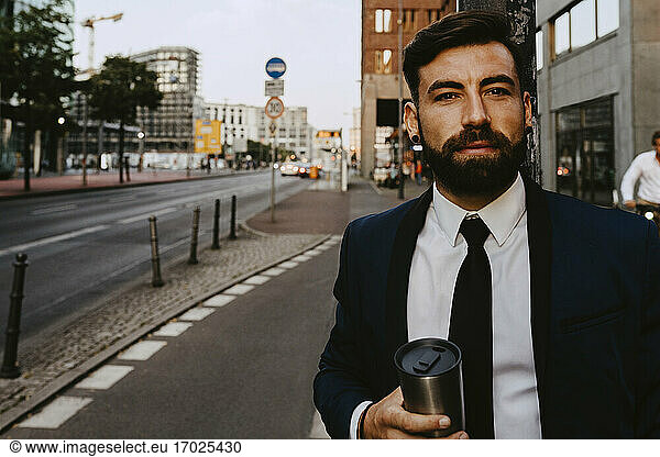 Portrait of businessman with insulated drink container standing on footpath