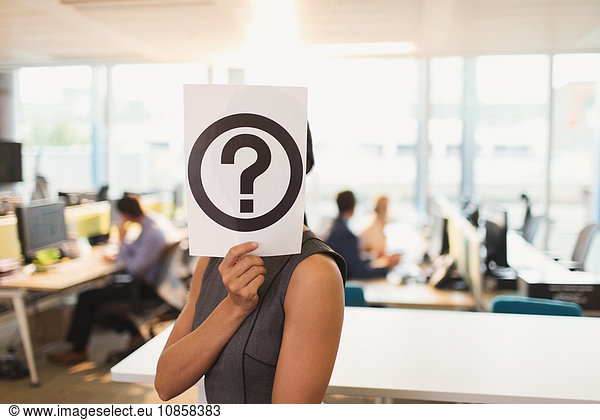 Portrait of businesswoman holding question mark printout over her face in office