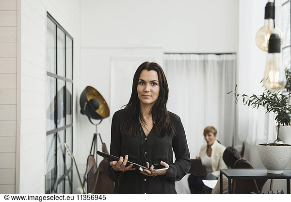 Portrait of businesswoman holding technologies with people in background