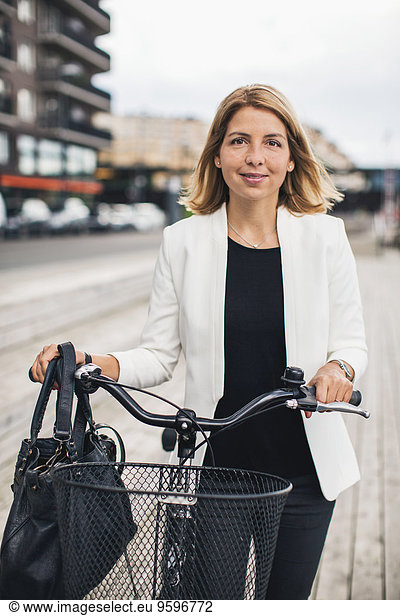 Portrait of businesswoman standing with bicycle in city