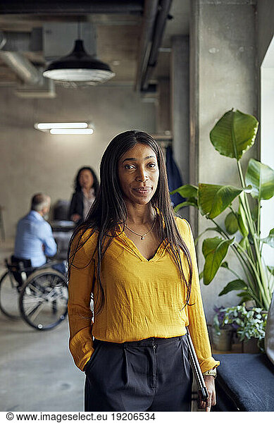 Portrait of businesswoman standing with laptop at creative office