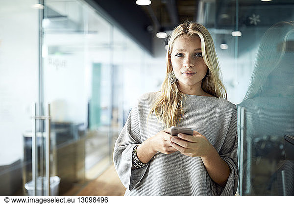 Portrait of businesswoman using mobile phone while standing at corridor