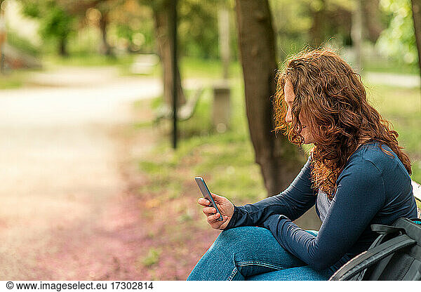 Portrait of charming red haired young woman with smartphone in a park