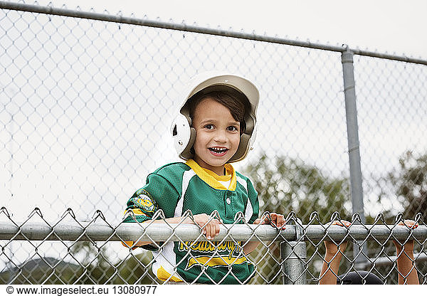 Portrait of cheerful boy in baseball uniform against clear sky